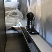 A black metal bed rail plunger mounted on a white surface, part of a camping trailer's bed locking mechanism.