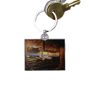 A keychain with a rectangular chalk art design depicting an outdoor scene with a camper.