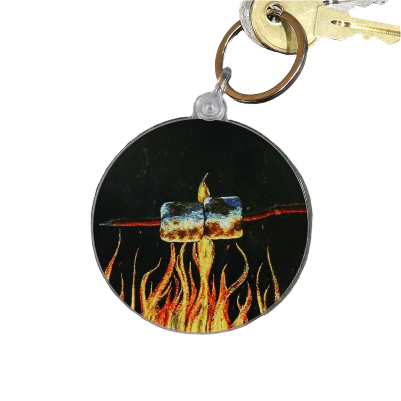 A keychain with a circular tag featuring an illustration of a marshmallow on fire against a black background, attached to a pair of keys.
