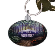 A keychain with a printed image of a camping scene with trees and a camper.