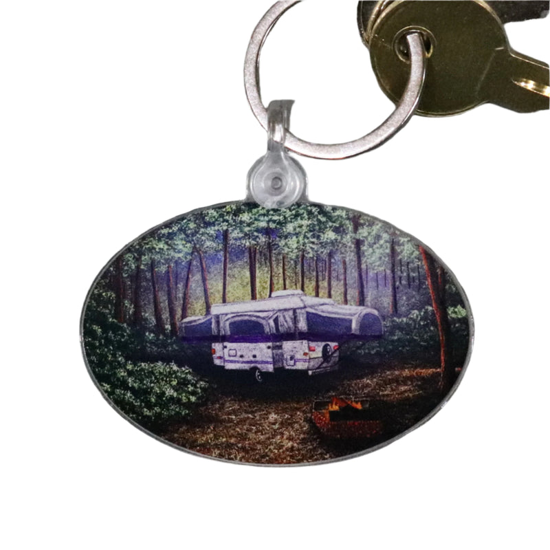 A keychain with a printed image of a camping scene with trees and a camper.
