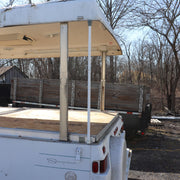 An adjustable metal roof support pole installed on a pop-up camper, with the camper set against a outdoor backdrop.