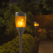NEBO branded solar torches with a warm light glow installed in a garden setting.