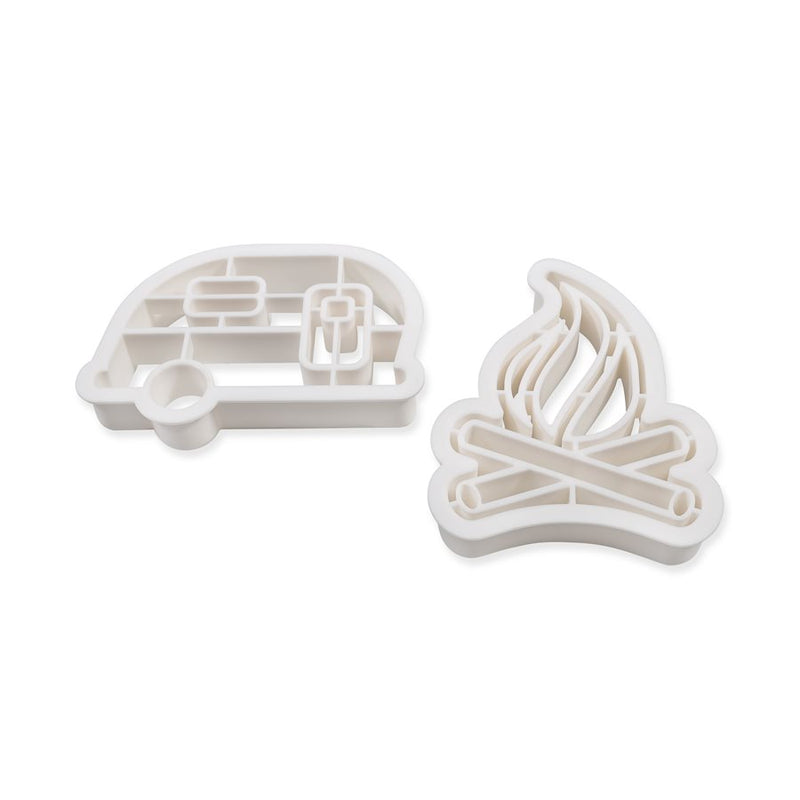 Two white plastic cookie cutters, one in the shape of an RV and the other in the shape of a campfire.