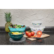 A set of four multicolored nesting bowls with a camping design, displayed with a small bowl on top, followed by a medium, large, and x-large bowl nested within each other. The bowls are on a kitchen counter with a pineapple and some sliced tomatoes in the background.