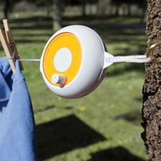 A portable white laundry reel with an yellow top, attached to a tree with a blue shirt hanging on it.