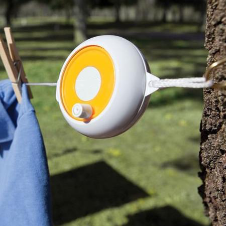 A portable white laundry reel with an yellow top, attached to a tree with a blue shirt hanging on it.