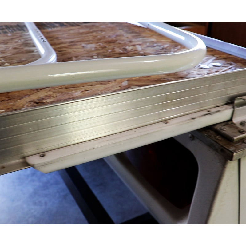 A close-up image of a white plastic bed slide rail attached to a mechanism, presumably part of a recreational vehicle's bed extension system.